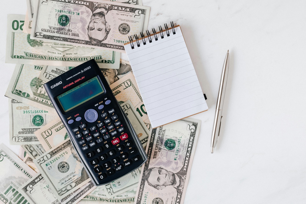 Calculator and Notepad placed over a Stack of Paper Bills
