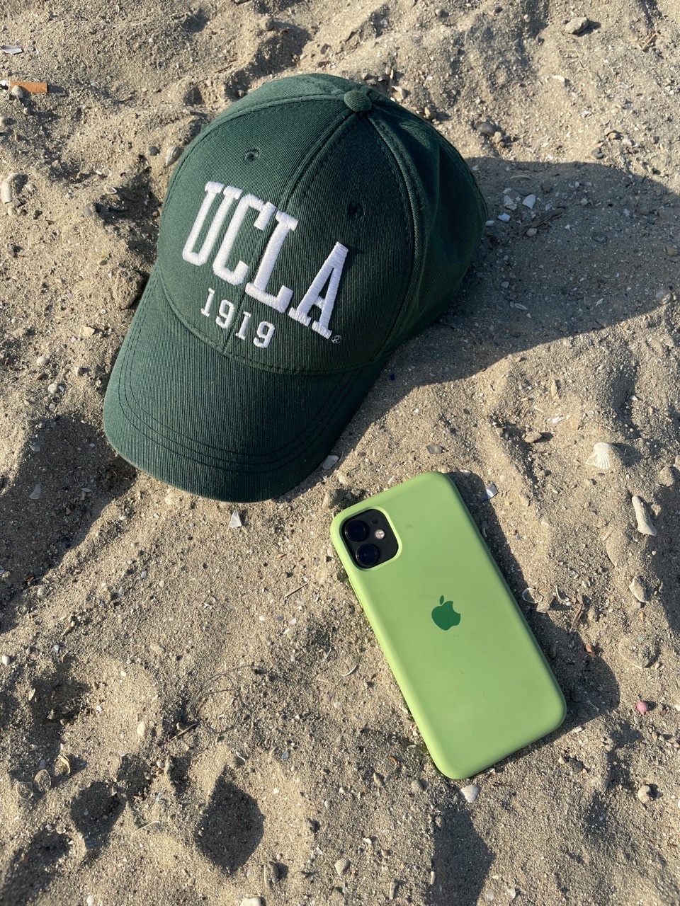 Green Cap of UCLA and Smartphone on Sand
